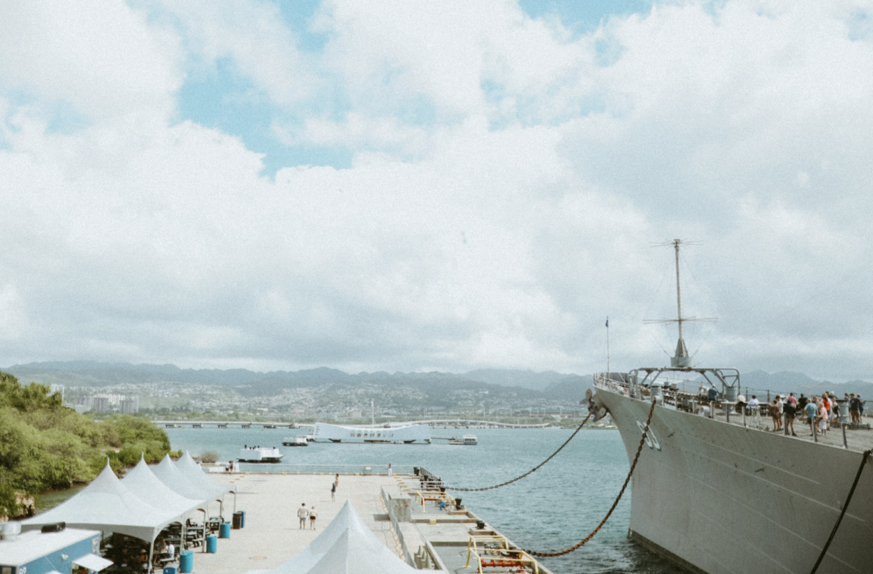 The USS Missouri battleship moored at Pearl Harbor with the USS Arizona Memorial and the Oahu shoreline in the background